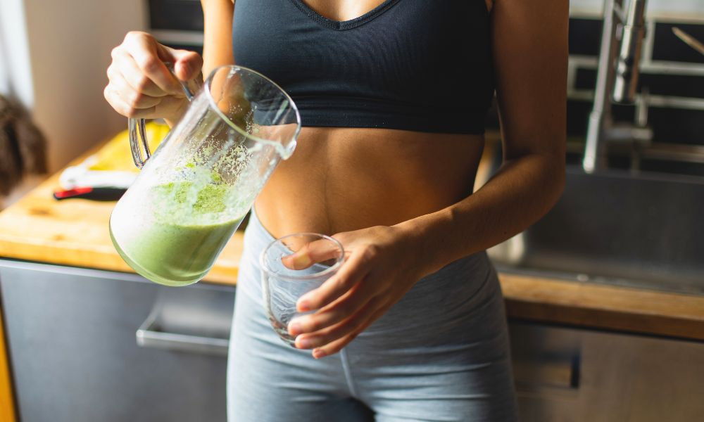  Žena nalieva zelený smoothie do pohára – detoxikácia a zdravé nápoje na podporu trávenia a chudnutie.
