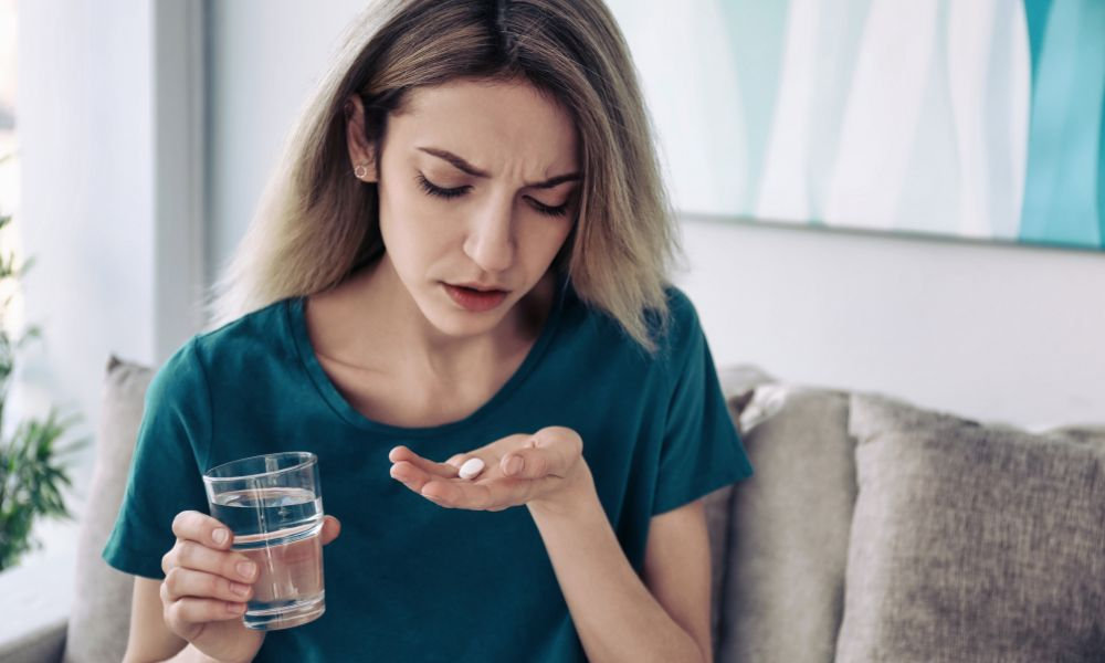  Tabletka po styku – žena si prezerá tabletku pred užitím so sklom vody v ruke