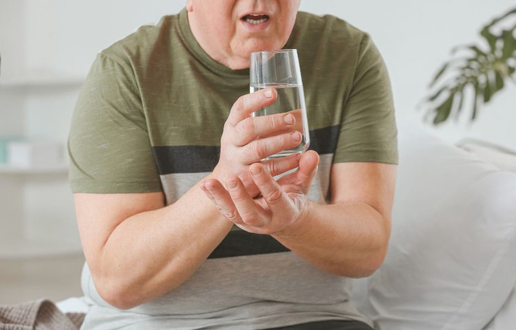 Muž s trasúcou sa rukou držiaci pohár vody – čo je Parkinsonova choroba a jej viditeľné symptómy.