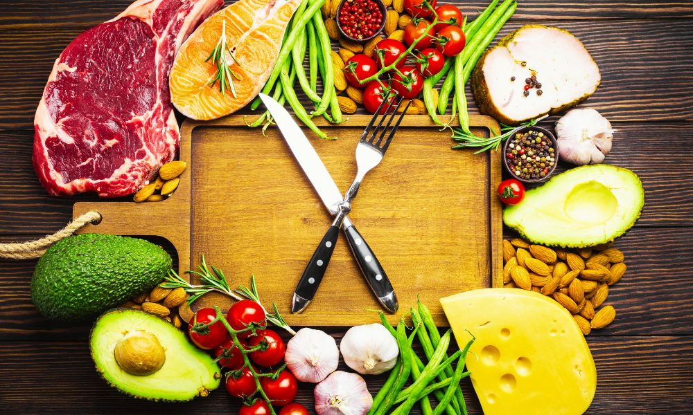  Výber čerstvých keto potravín na drevenej doske vrátane mäsa, zeleniny, avokáda a syra – keto diéta potraviny a vhodné ingrediencie.
