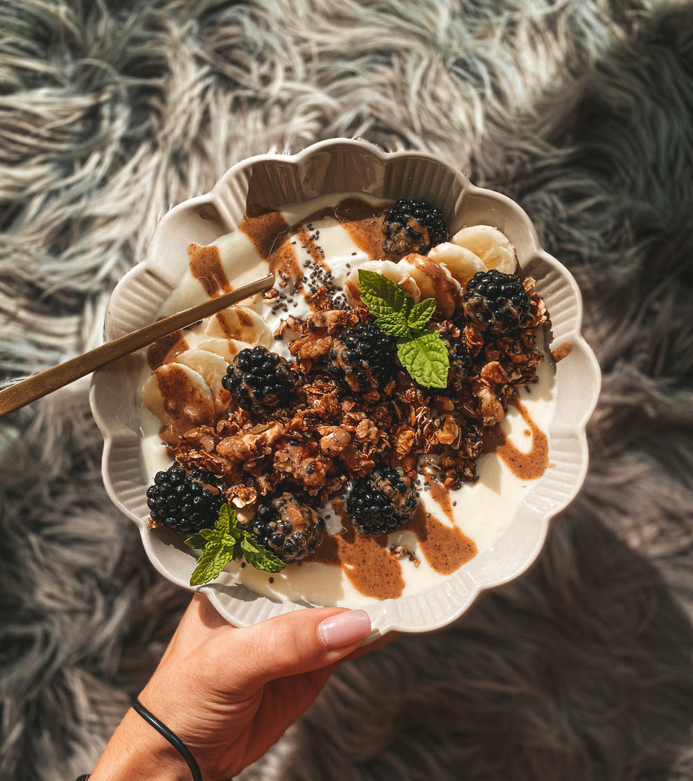  Tip na servírovanie - granola s ovocím – Biela miska s jogurtom, granolou, černicami, banánom a orieškami, zdobená lístkami mäty.