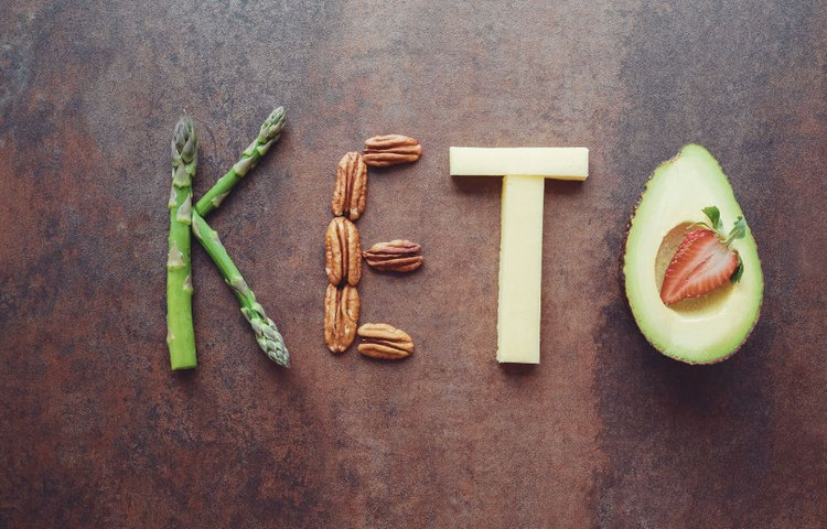 Slovo "KETO" vytvorené z rôznych potravín ako špargľa, orechy, syr a avokádo – keto diéta potraviny a ich pestrosť
